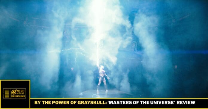 Person standing center stage amid blue smoke and a bright vertical light beam, creating a dramatic sci‑fi performance look, with a black/gold banner below reading 'BY THE POWER OF GRAYSKULL...'],