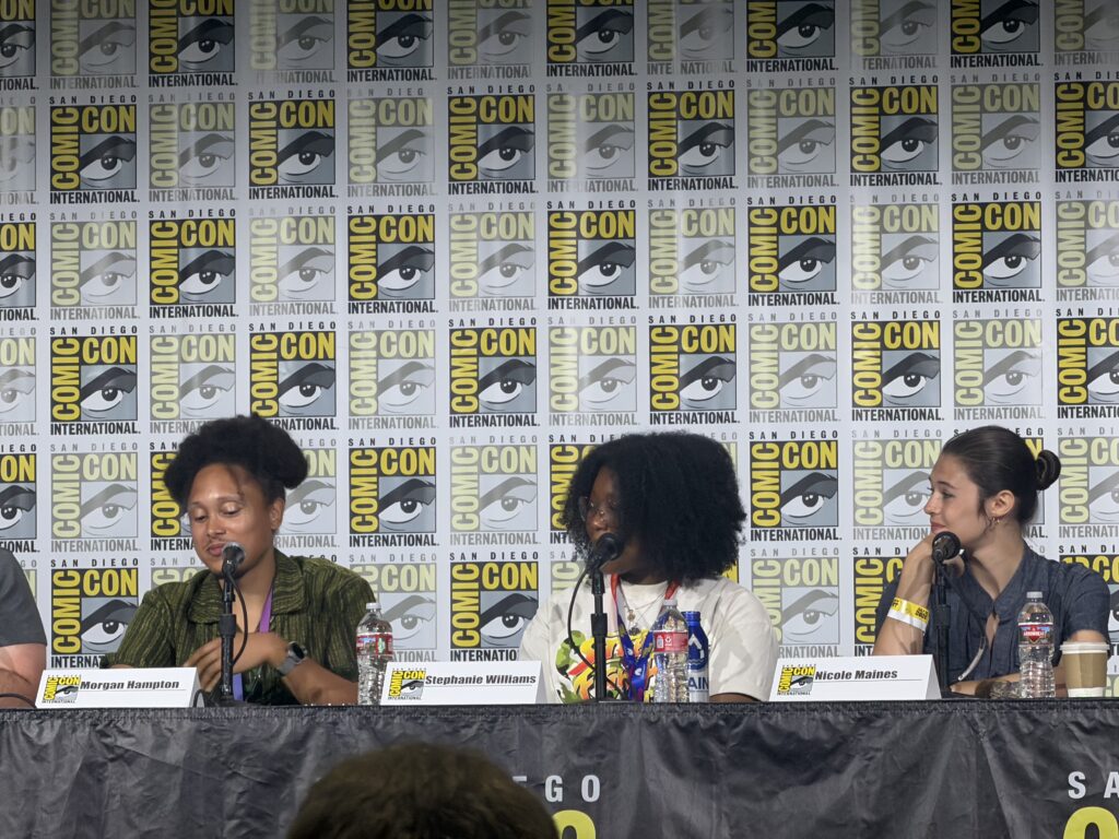 Panelists at Comic-Con International San Diego, seated at a long table with nameplates for Morgan Hampton, Stephanie Williams, and Nicole Maines.
